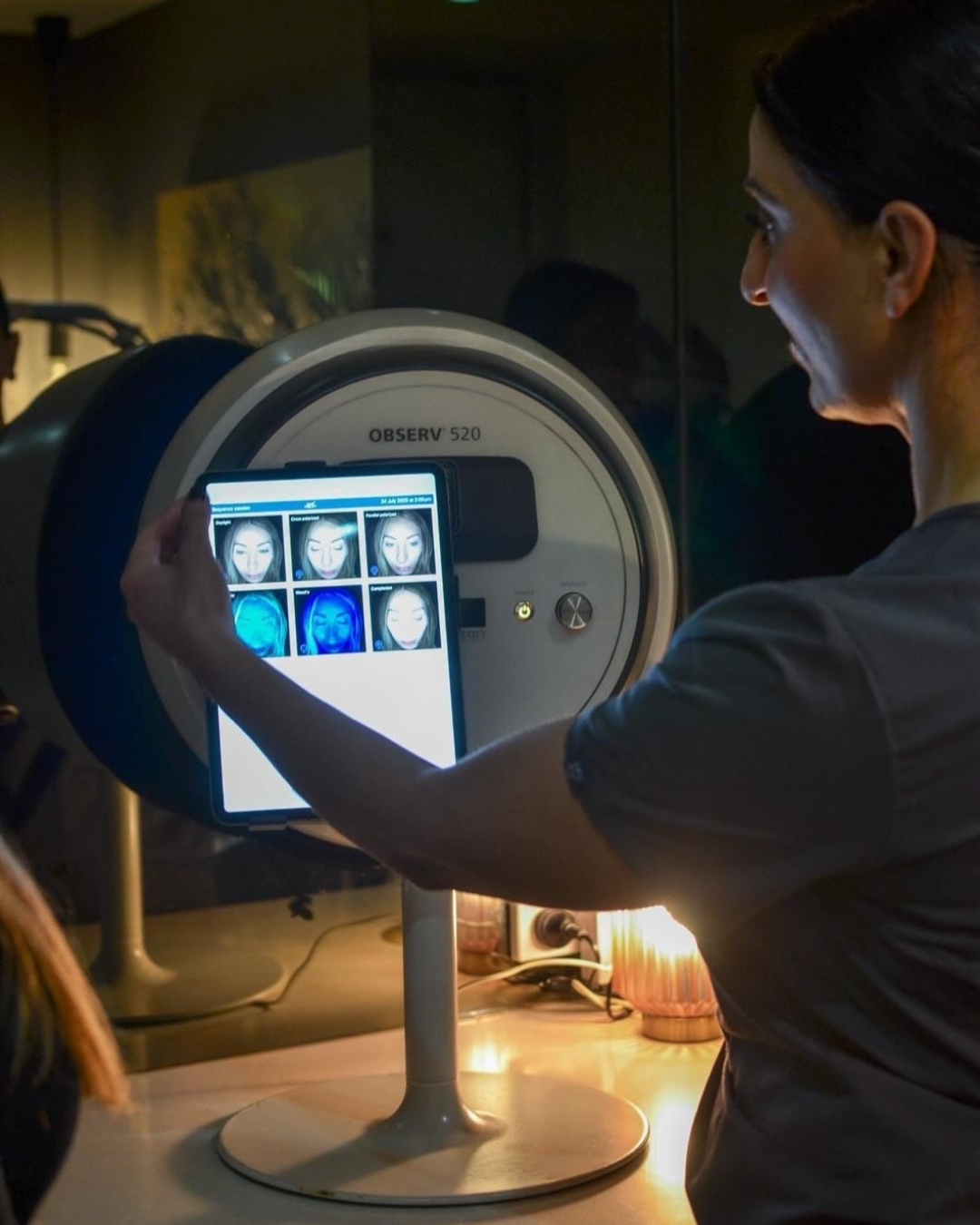 Person using the Observ 520 device with a screen displaying images of facial consultation in a dimly lit room.